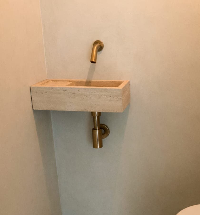 Travertin fonteintje aan de wand in een toilet, met gouden wandkraan